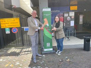 Wethouder René van Ginderen en GroenLinks raadslid Chahira Mediani nemen de eerste zonnebrandpaal in Roosendaal in gebruik.