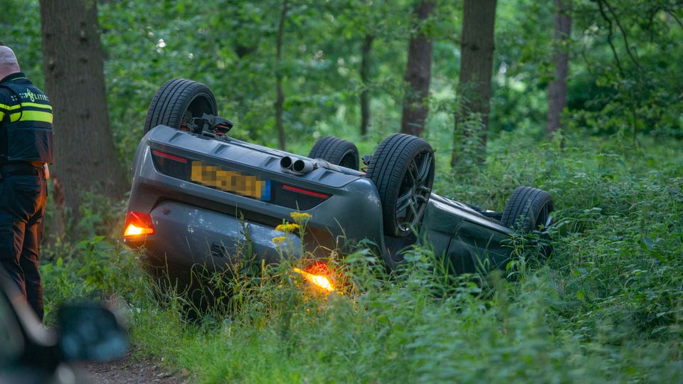 Achterkant auto met knipperlichten aan, op de kop in een met veel groen begroeide sloot
