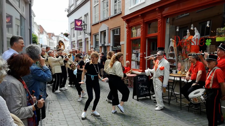 Publiek kijkt lachend toe als straatorkest en danseressen door smalle straat van Bergen op Zoom trekken