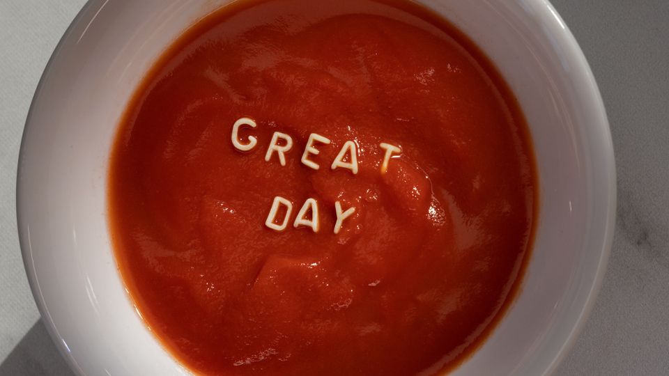 Witte soepkom met tomatensoep en letters van vermicelli die 'great day' spellen