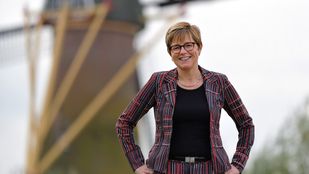 Miranda de Vries in gestreept rood-bordeauxrood pak poseert bij een molen