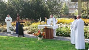 Eucharistieviering in de open lucht met pastoor achter altaar naast het gazon met volwassen misdienaars aan weerszijden