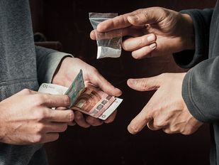 Close-up van drugsdeal tussen twee mensen waarbij je alleen de handen ziet en geld wordt betaald voor een zakje drugs