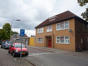 Voorgevel in gele bakstenen en rode deur van buurthuis Keijenburg in Roosendaal