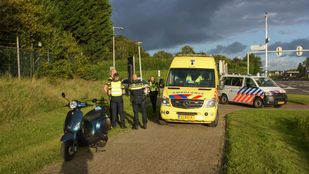 Op een fietspad naast een greppel staat een scooter met daarachter een ambulance, politiewagen en enkele hulpverleners