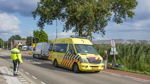 Agent regelt het verkeer, aan de overkant van de weg staan een ambulance en een witte bestelbus en naast de ambulance ligt een scooter in het gras