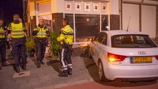 Drie agenten staan naast een witte auto die zich in de gevel van een hoekwoning heeft geboord.