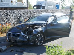 Donkere Audi met zwaarbeschadigde ingedeukte neus staat met beide deuren open midden op de weg en voor de auto liggen onderdelen van een andere auto, zoals een uitlaat