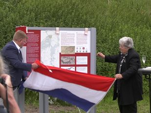 Patrick van der Velden en Ans van den Berg staan aan weerzijden van een informatiepaneel en onthullen deze door het weghalen van de Nederlandse vlag