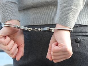 Close-up van handen die op de rug in handboeien zitten