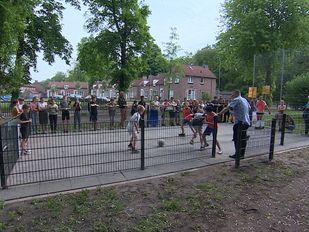 Tientallen kinderen staan op en rond een met hekken omringd voetbalcourt