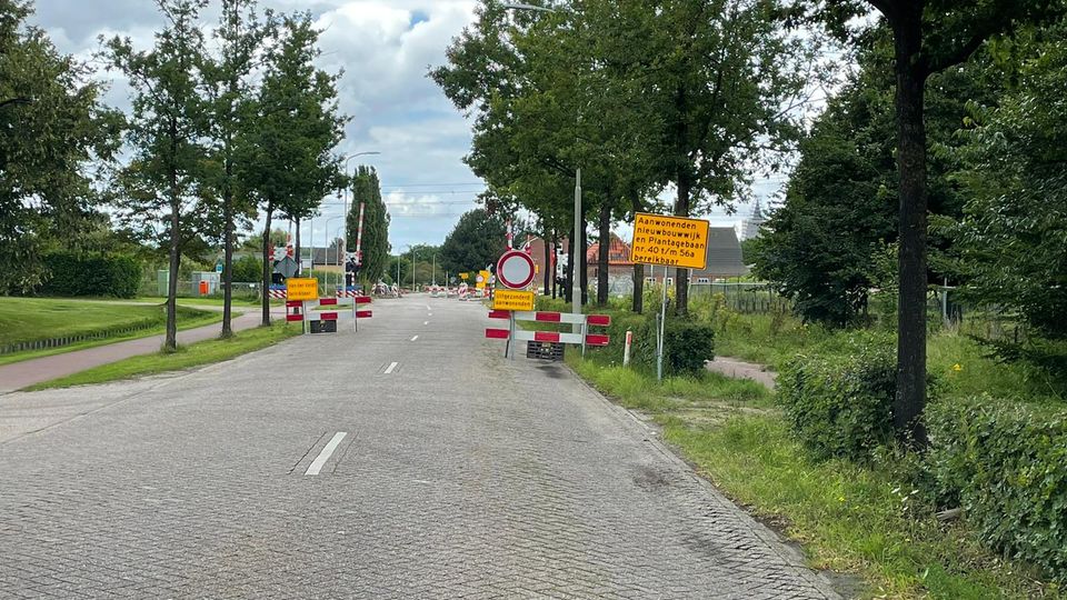 Gele verkeersborden met informatie over wegafsluiting bij rood-wit-geblokte hekken