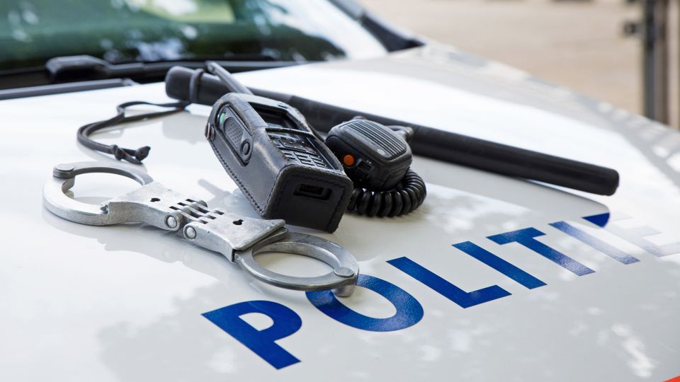 Handboeien, wapenstok en portofoon op motorkap van politiewagen