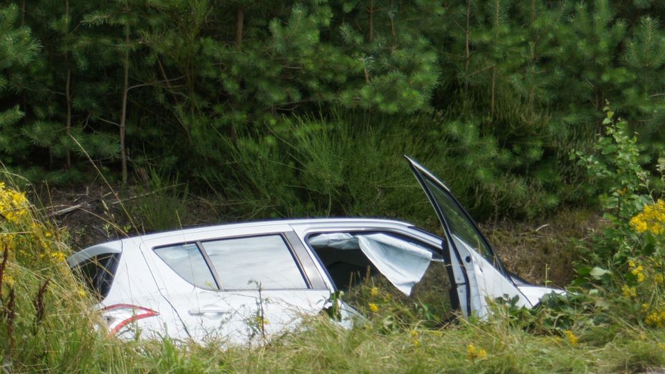 Zijkant van een auto met de passagiersdeur open steekt nog net boven de slootkant uit