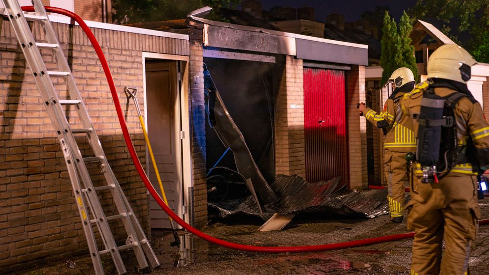 Twee brandweermensen staan bij een uitgebrande garagebox