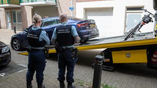 Twee marechaussees kijken toe hoe een auto op een oplegger wordt gereden