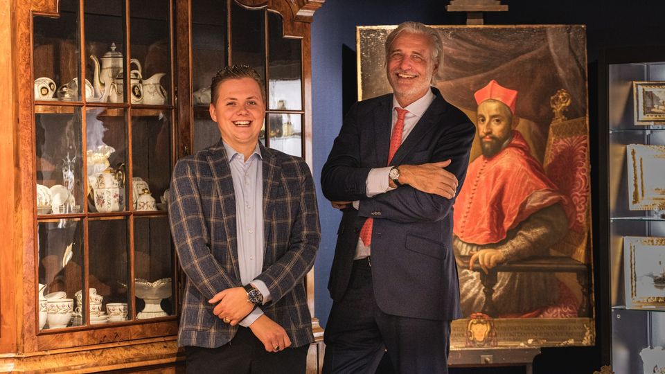 Bram Bouwens staat links met daarnaast Mark Haasnoot met achter hen een kast vol antiek porselein en een antiek portretschilderij