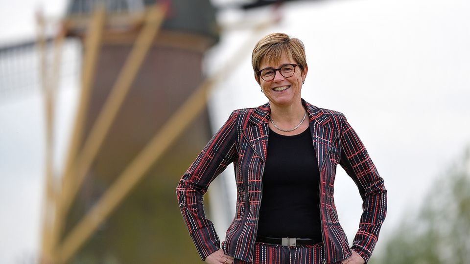 Miranda de Vries in gestreept rood-bordeauxrood pak poseert bij een molen