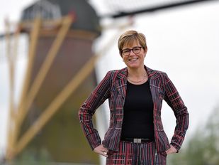 Miranda de Vries in gestreept rood-bordeauxrood pak poseert bij een molen