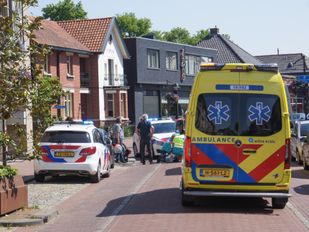 Een ambulance en twee politie-auto's staan rondom ambulancemedewerkers die midden op straat iemand behandelen