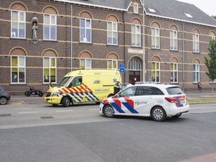 Motor staat op trottoir met daarnaast een gele ambulance en op de voorgrond een witte politiewagen