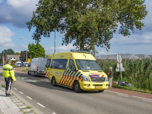 Agent regelt het verkeer, aan de overkant van de weg staan een ambulance en een witte bestelbus en naast de ambulance ligt een scooter in het gras