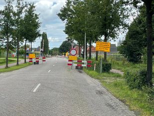 Gele verkeersborden met informatie over wegafsluiting bij rood-wit-geblokte hekken