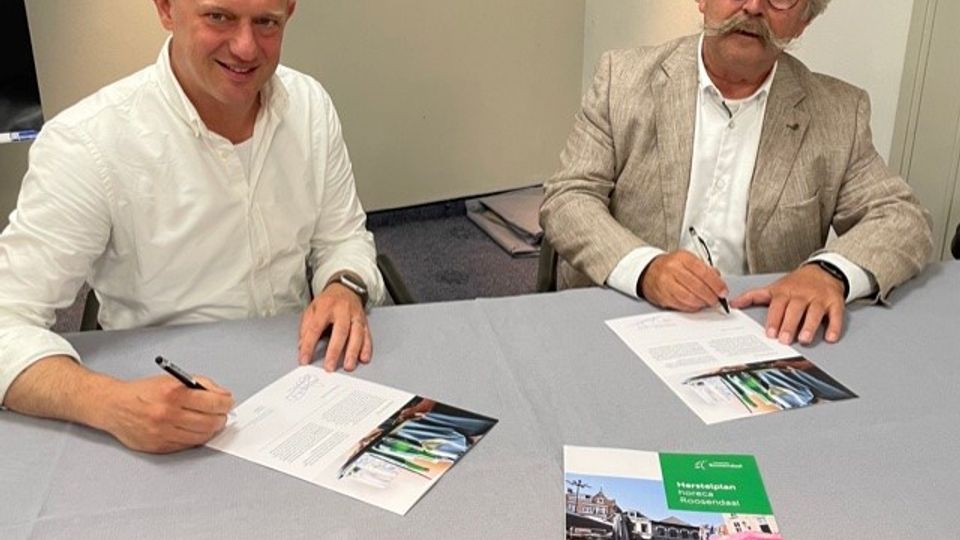 Koen Bakker van Koninklijke Horeca Nederland Roosendaal ondertekent een formulier en rechts naast hem kijkt wethouder Cees Lok toe