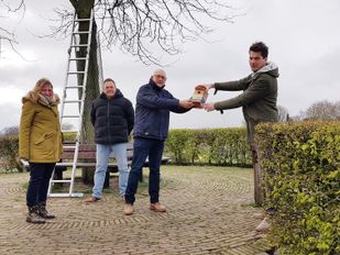Marjolein van Put en Herman Heyns kijken toe hoe Gerard van den Bergh een vogelhuisje geeft aan wethouder Jeffrey van Agtmaal