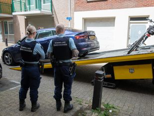 Twee marechaussees kijken toe hoe een auto op een oplegger wordt gereden