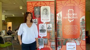 Anneke Wijn in een witte bloes staat voor oranje banners met daarop oude foto's en teksten over Roosendaal