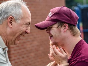 Oudere man en jongen met syndroom van Down staan lachend tegenover elkaar