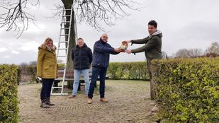 Marjolein van Put en Herman Heyns kijken toe hoe Gerard van den Bergh een vogelhuisje geeft aan wethouder Jeffrey van Agtmaal