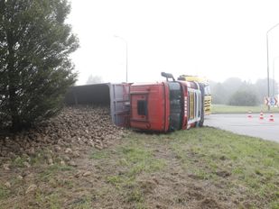 Vrachtwagen met rode cabine ligt op z'n kant naast rotonde en uit de laadbak komt een stroom aan suikerbieten