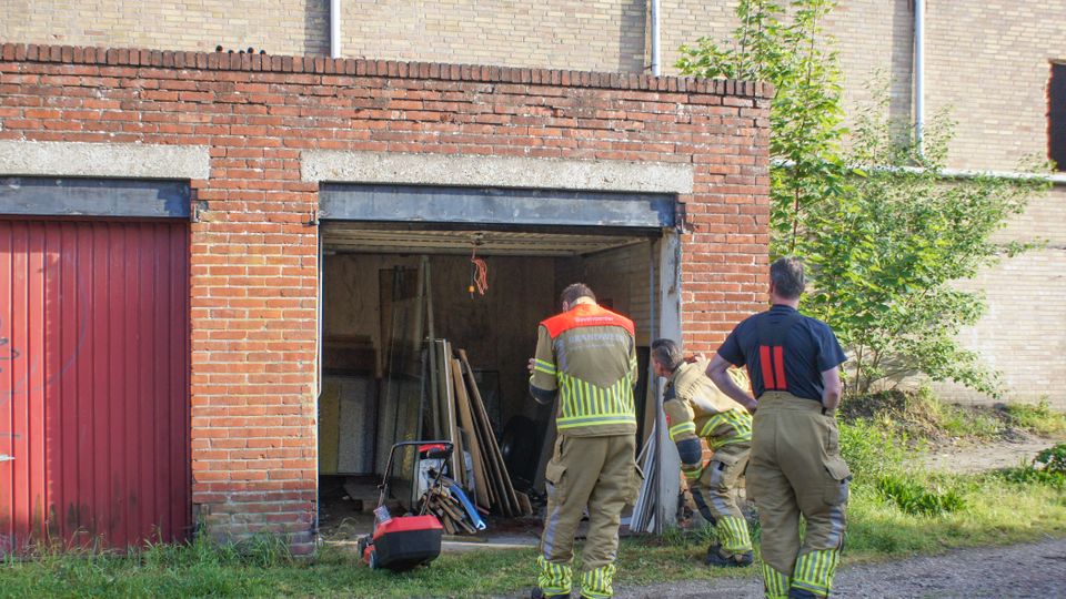 Brandweermensen staan voor een open garagebox