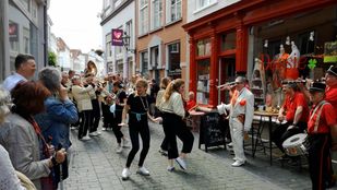 Publiek kijkt lachend toe als straatorkest en danseressen door smalle straat van Bergen op Zoom trekken