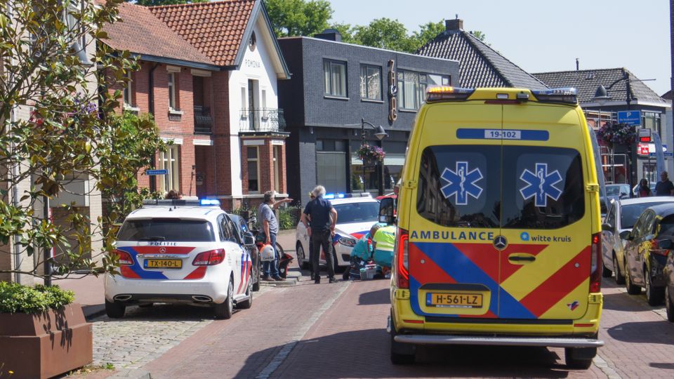 Een ambulance en twee politie-auto's staan rondom ambulancemedewerkers die midden op straat iemand behandelen