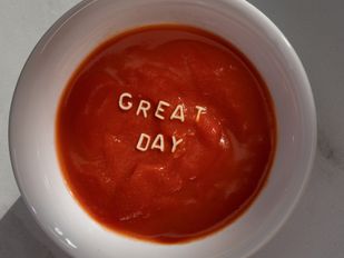 Witte soepkom met tomatensoep en letters van vermicelli die 'great day' spellen