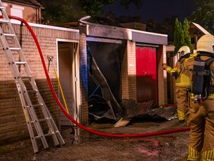 Twee brandweermensen staan bij een uitgebrande garagebox