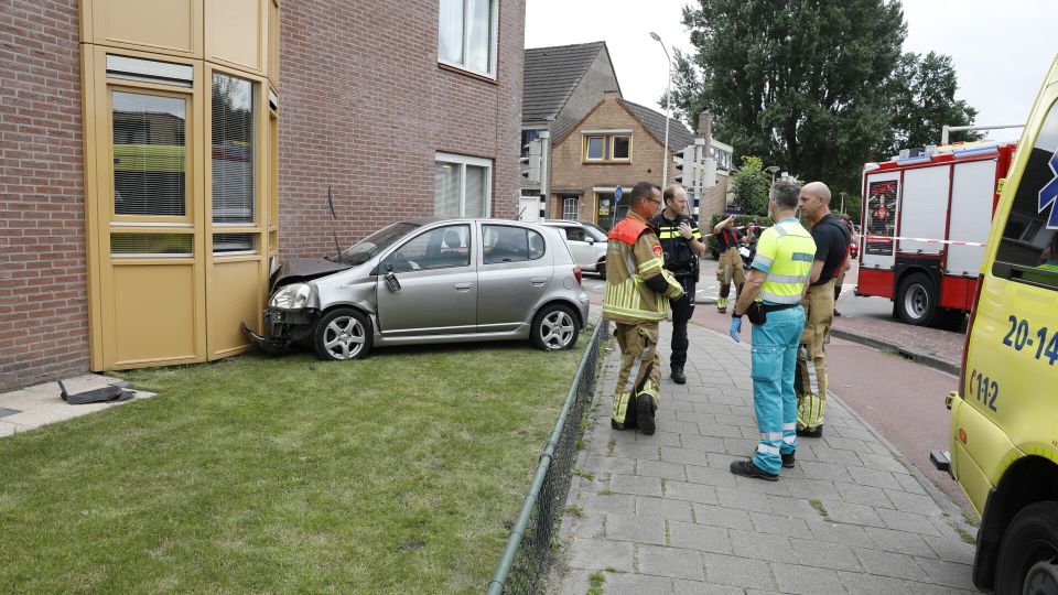Zilverkleurige auto staat met de neus in de gevel van een appartementencomplex en hulpverleners staan er omheen