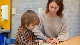 Vrouw kijkt mee met peuter die aan tafel zit te tekenen