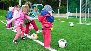 Kleuters in felroze kleren proberen voetballen weg te trappen