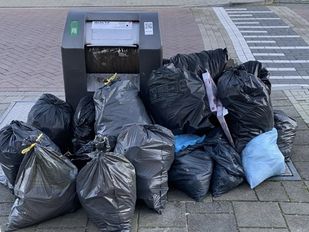 Volle vuilniszakken opgestapeld tegen afvalbak