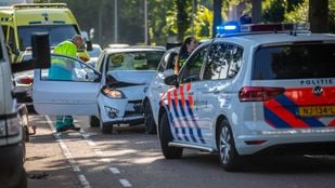 Op de voorgrond een politieauto, op de achtergrond een ambulance en daartussen twee witte auto's waarvan eentje een in elkaar gedeukte neus heeft. Een ambulancemedewerker staat naast de open deur van de gedeukte auto en kijkt naar binnen.