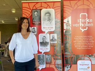 Anneke Wijn in een witte bloes staat voor oranje banners met daarop oude foto's en teksten over Roosendaal