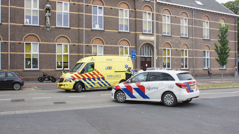 Motor staat op trottoir met daarnaast een gele ambulance en op de voorgrond een witte politiewagen