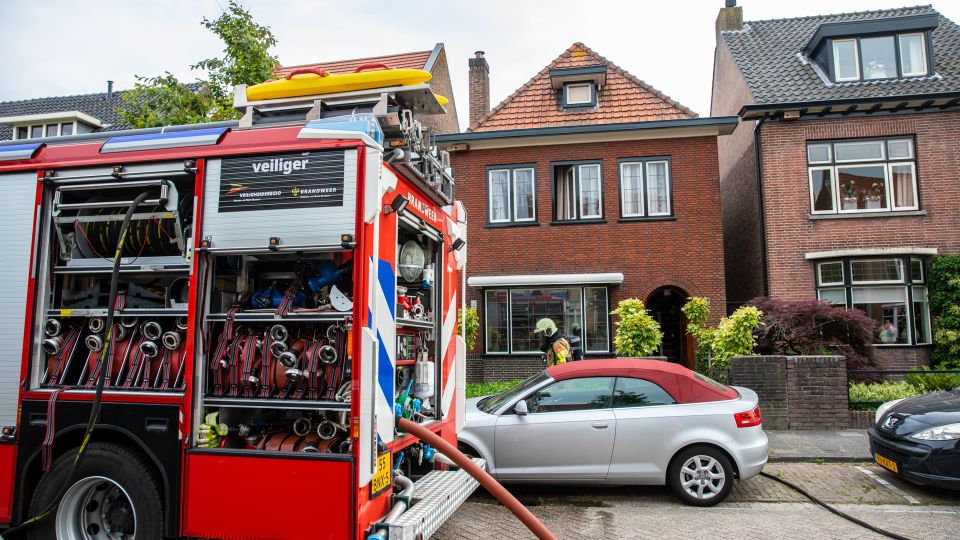 Brandweerwagen voor woningen met hulpverleners in de deuropening van het middelste huis
