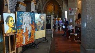 Grote schilderijen staan op schildersezels in het middenschip van een kerk