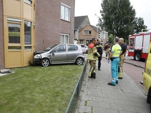 Zilverkleurige auto staat met de neus in de gevel van een appartementencomplex en hulpverleners staan er omheen