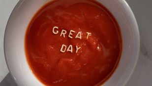 Witte soepkom met tomatensoep en letters van vermicelli die 'great day' spellen